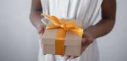 person holding a gift box with a decorative yellow ribbon.