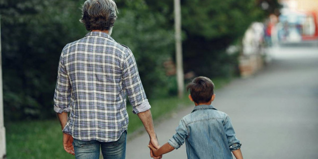 older man and young boy holding hands, seen from behind.