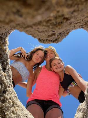 Melissa DiNapoli and her daughters at the beach, framed by a heart-shaped opening in the sand.