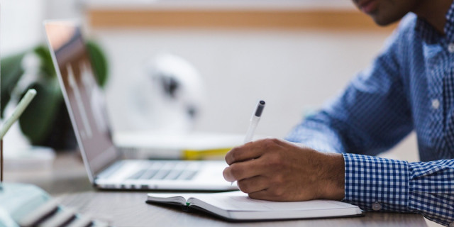 man writing while looking at laptop (detail).